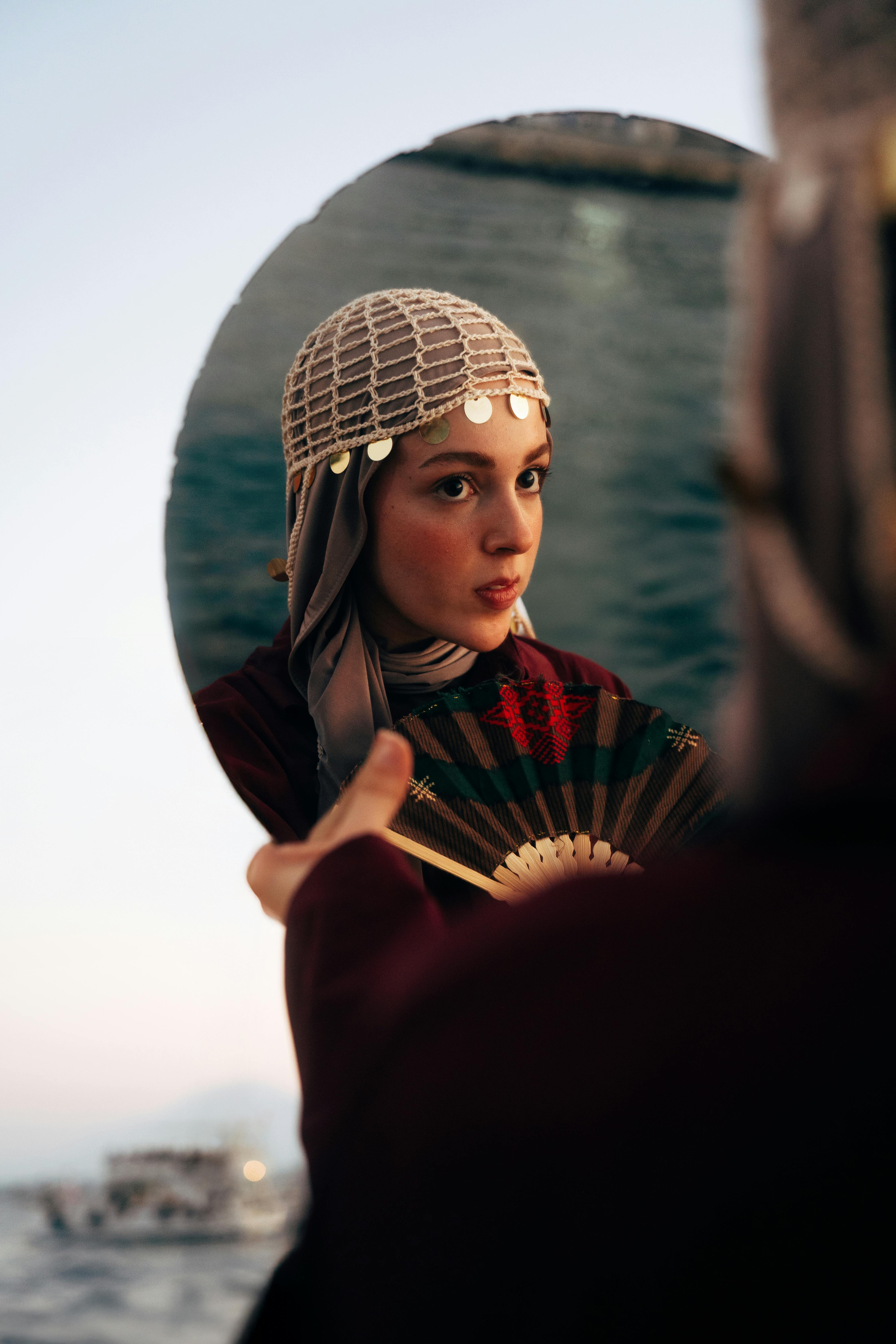 Captivating portrait of a woman with a fan, reflecting in a mirror at Antalya's beautiful coast during twilight.