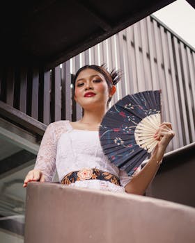 Stylish woman in traditional dress holding a fan outdoors, exuding elegance and grace.