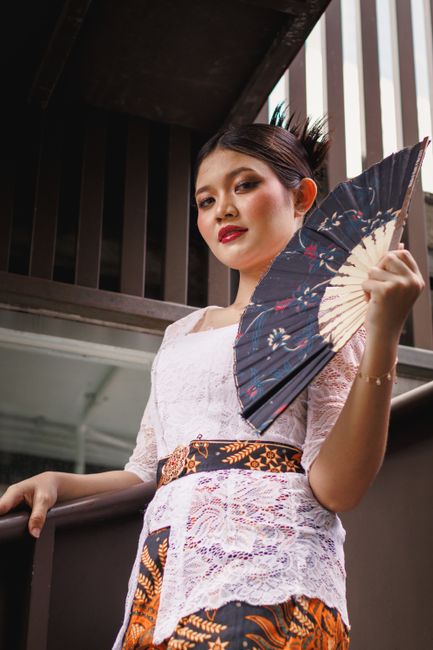 A woman in traditional attire holding a decorative fan, showcasing cultural elegance.