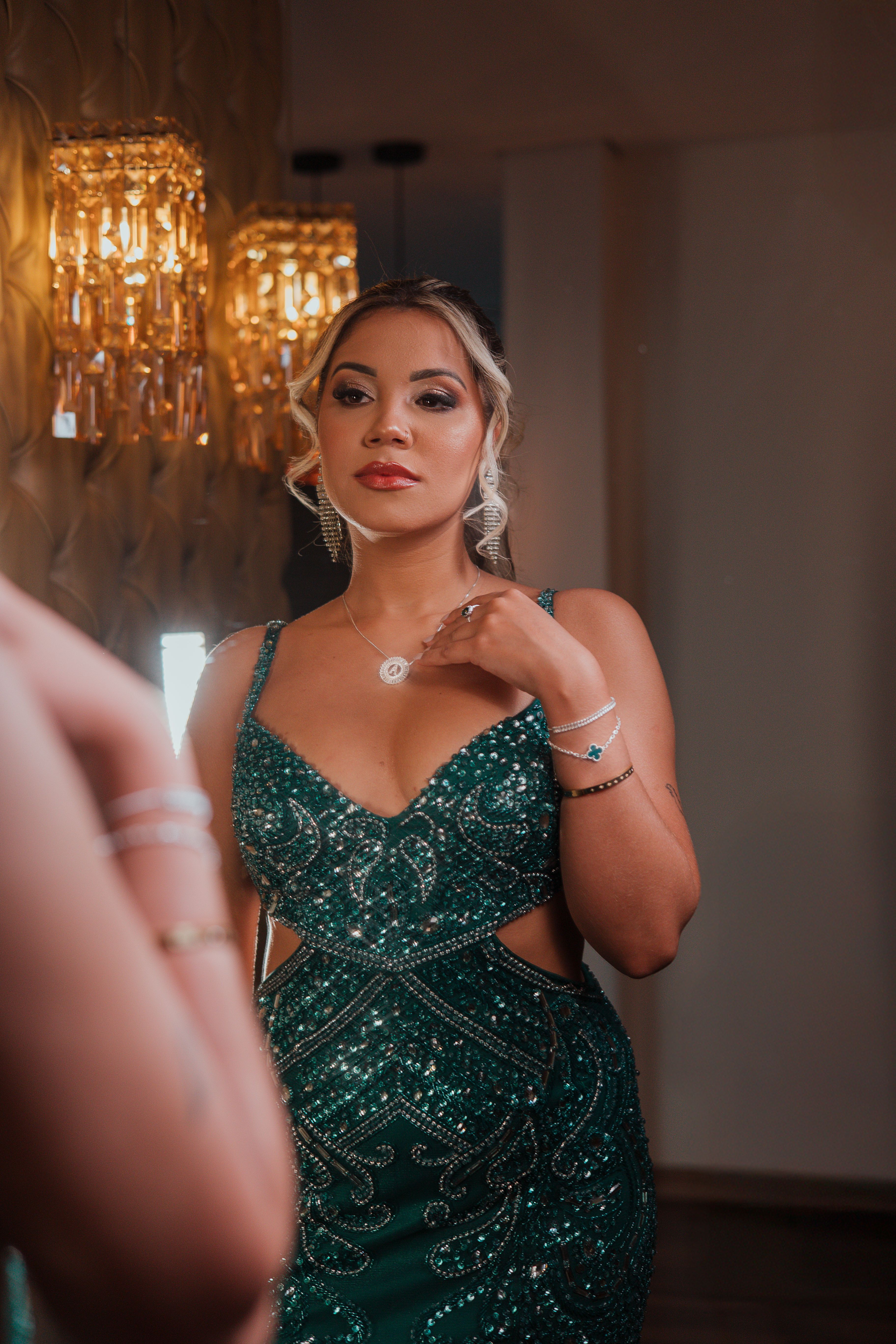Glamorous adult woman wearing a sparkling green dress, gazing into a mirror in a luxurious setting.