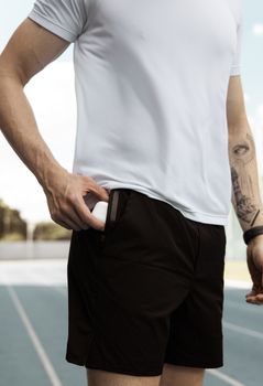 Close-up of a male athlete putting wireless earbuds in his pocket on a track field. Ideal for sports and lifestyle imagery.