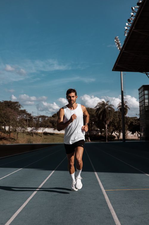 Free Fit adult male running on a track with blue sky background, promoting active lifestyle. Stock Photo