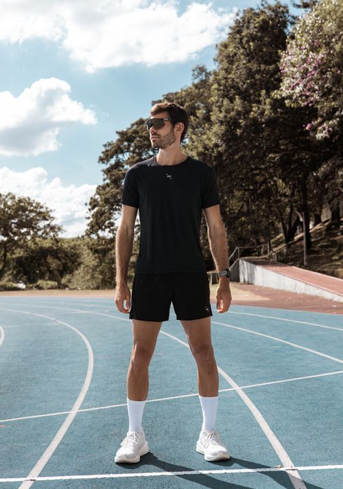 Free Young athlete standing on a track field surrounded by trees on a sunny day. Stock Photo