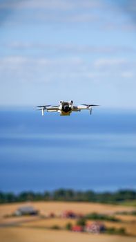 A drone flying over a coastal landscape with fields in the foreground and ocean in the background.