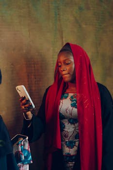 Woman in red hijab using smartphone indoors with a contemplative expression.