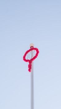 A traditional red wreath decorates a tall pole against a minimalistic clear sky.
