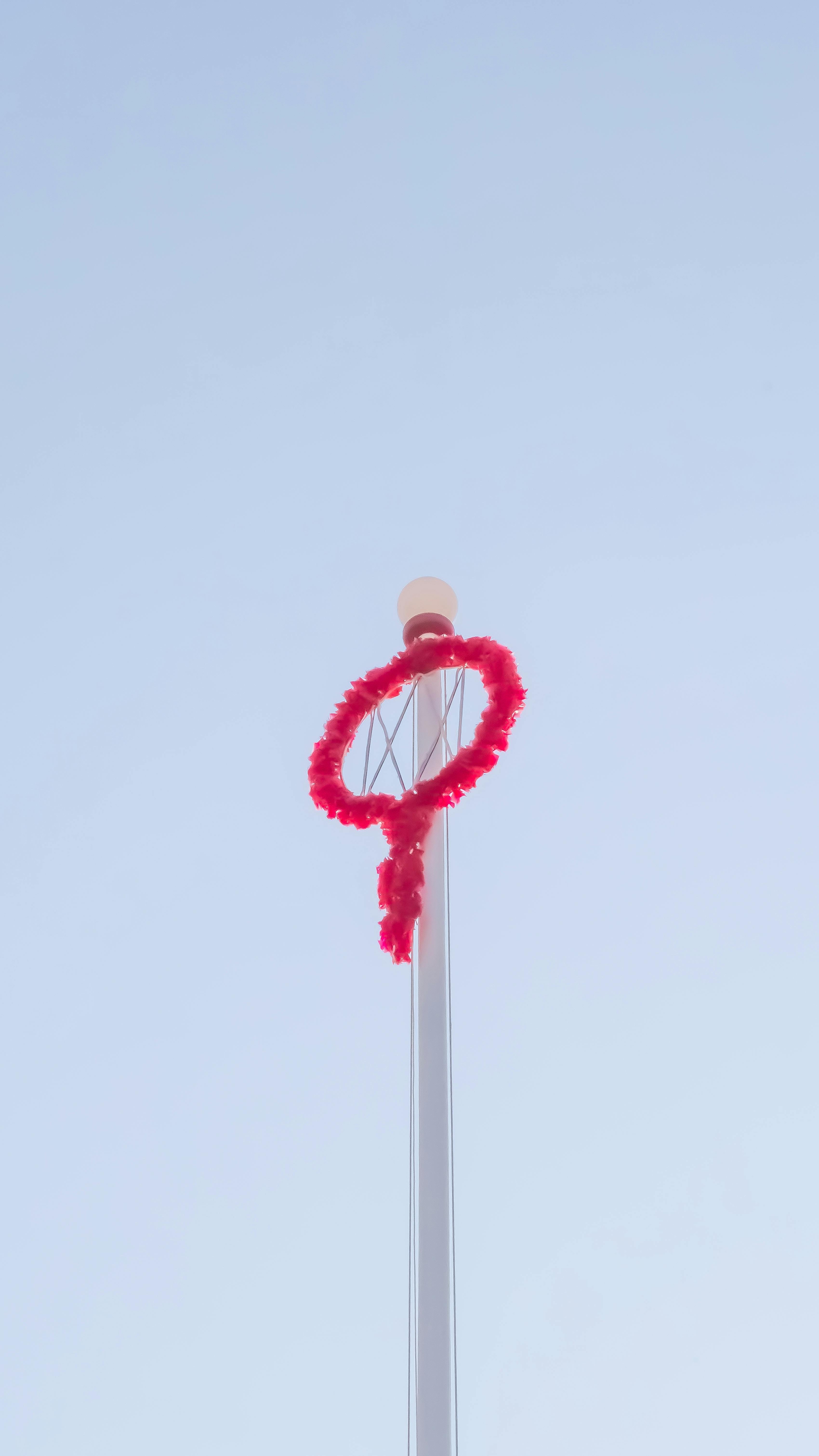 Gratis En traditionel rød krans dekorerer en høj stang mod en minimalistisk klar himmel. Lagerfoto