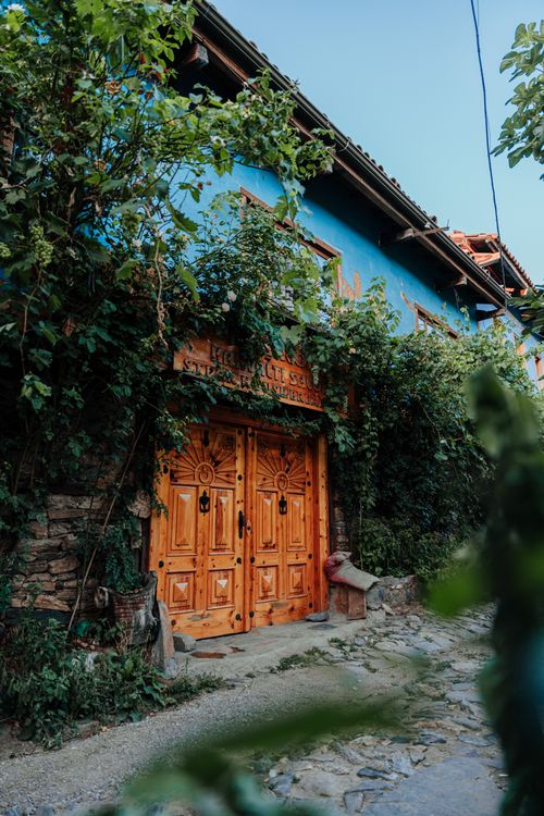 Free Rustic house with a vibrant blue facade and intricate wooden door surrounded by lush greenery. Stock Photo