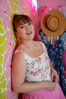 A smiling woman posing in a colorful retro-styled room with vibrant wallpaper and decor.