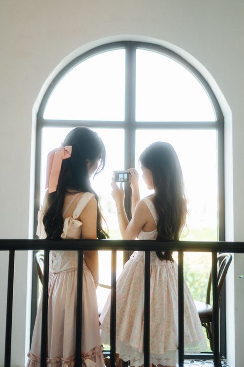 Free Two young women in elegant dresses capturing a moment by a bright window, offering a glimpse into casual lifestyle. Stock Photo