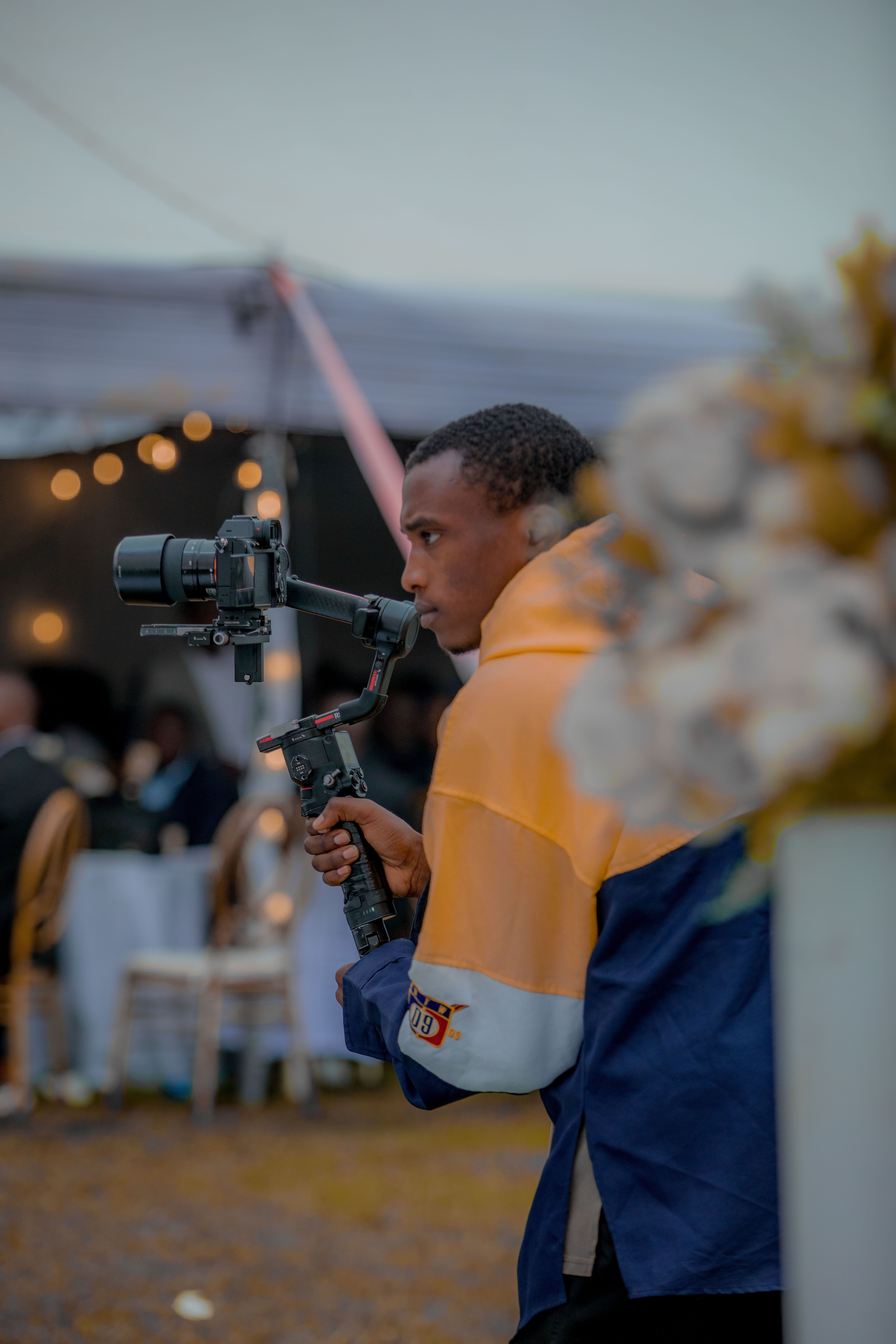 A videographer with camera gimbal filming an event setup outdoors.