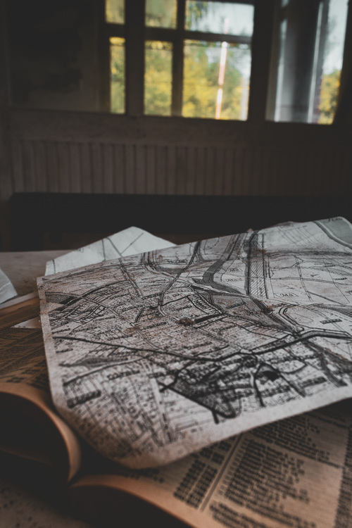 Free A vintage map laid on an open book in a dimly lit room with a window view. Stock Photo