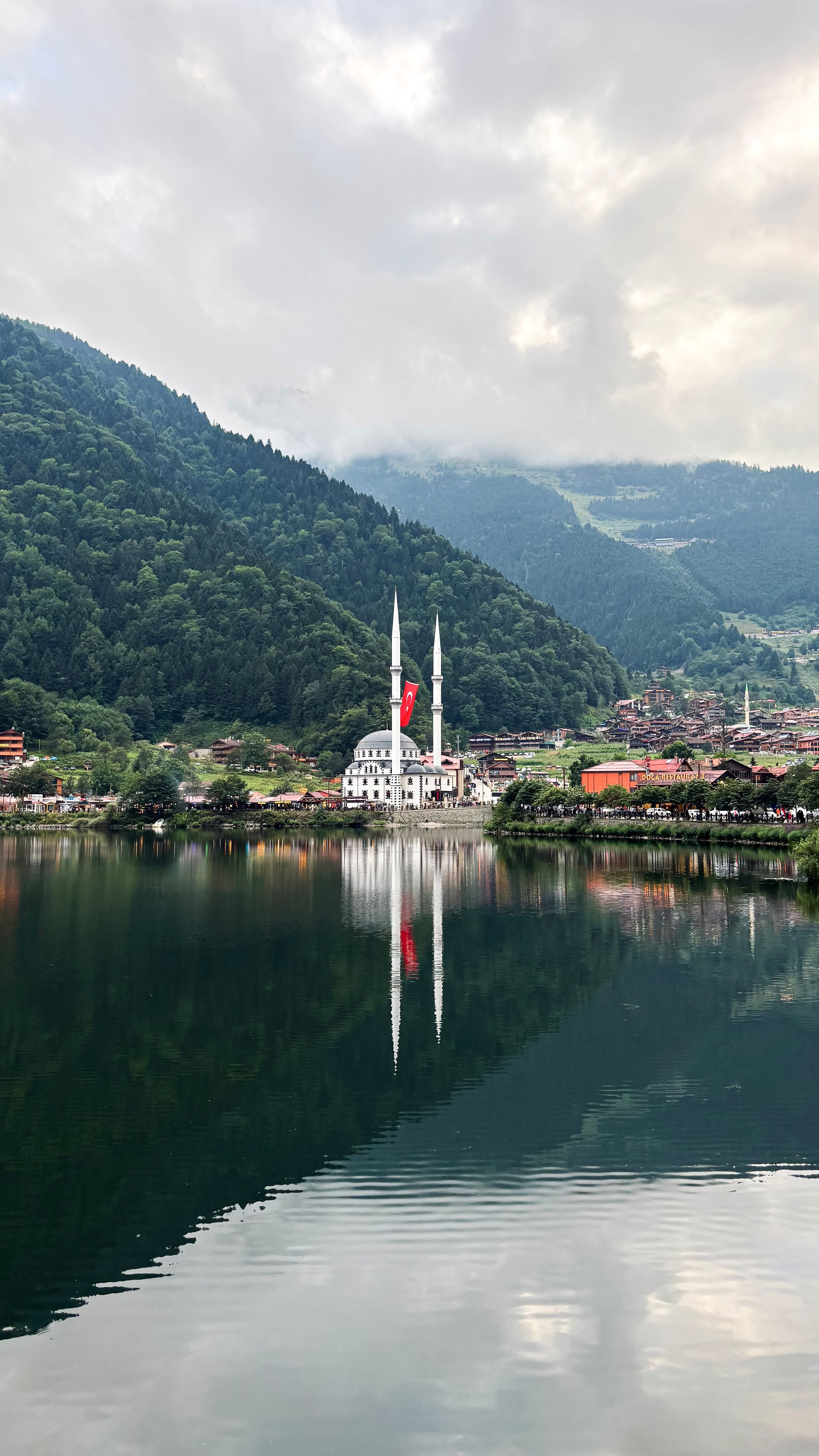 A picturesque view of a mosque reflected on a tranquil lake, surrounded by lush green mountains.