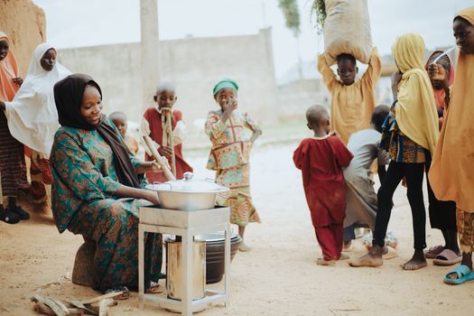 A lively scene of African children and a woman cooking outdoors in a community setting.