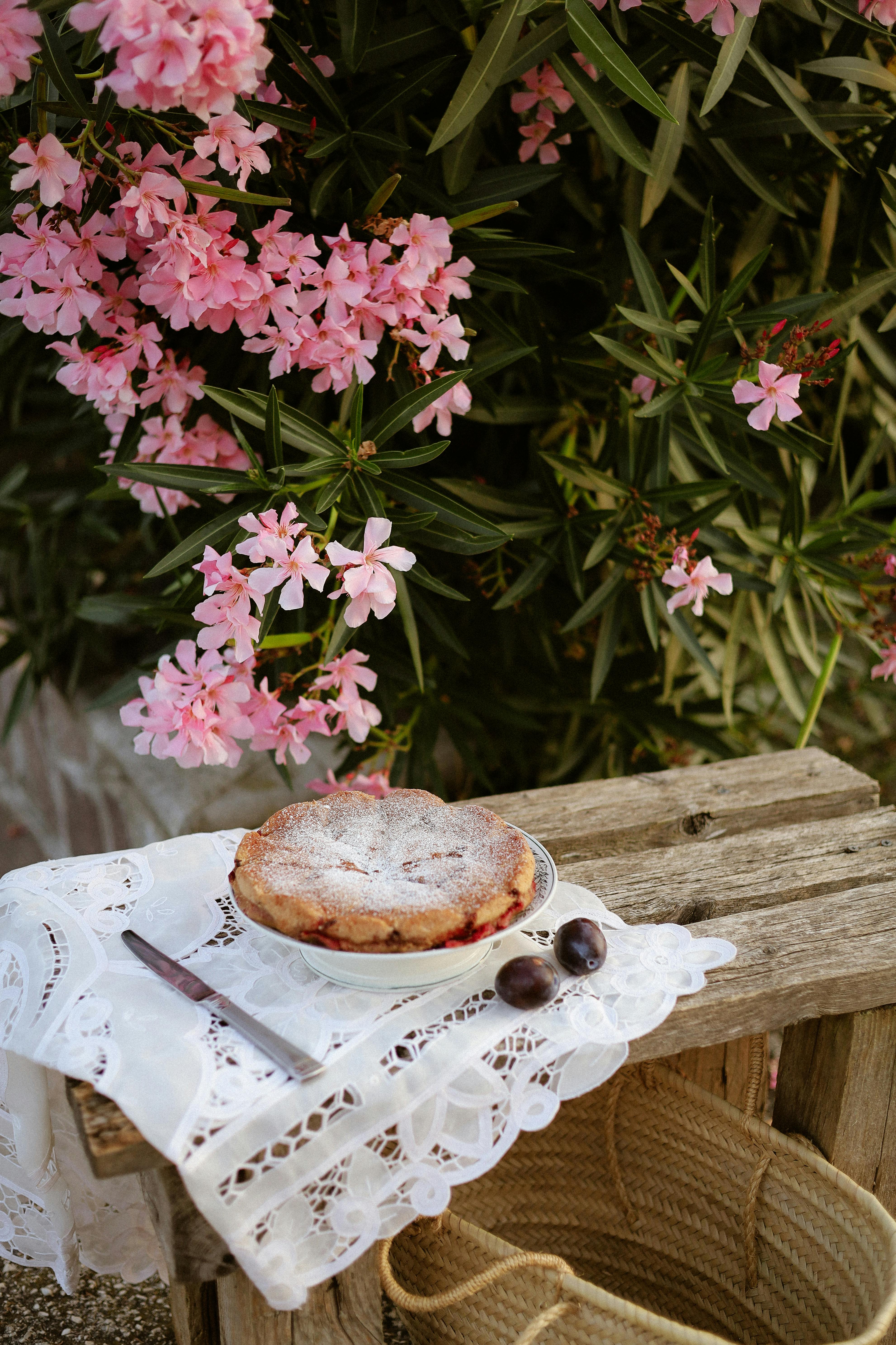 Homemade pie with fruits on a wooden bench surrounded by pink flowers, creating a rustic summer feel.