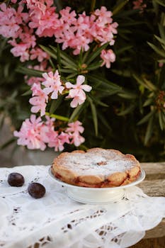 Delicious homemade pie on rustic table next to vibrant oleander flowers.