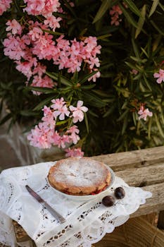 A delicious pie on a rustic table with pink oleander flowers creating a charming outdoor scene.
