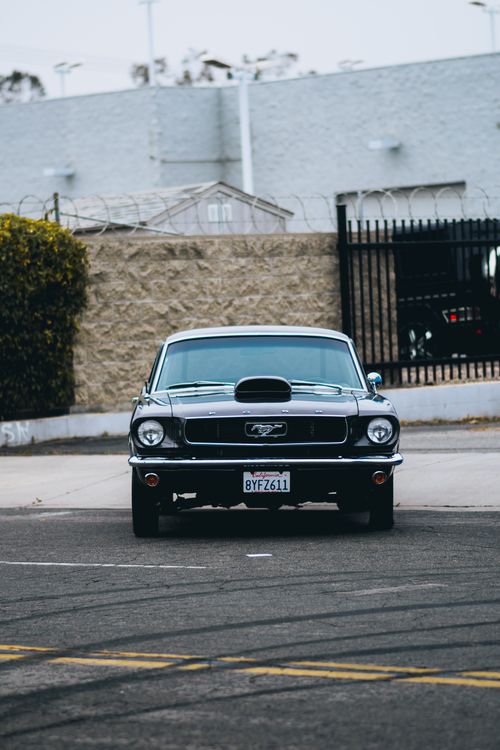 Free Vintage Ford Mustang parked on a city street, showcasing its classic design and American muscle car appeal. Stock Photo