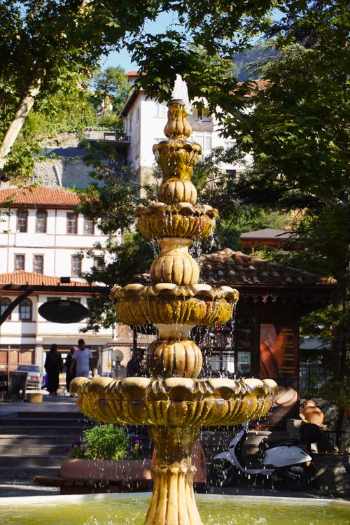 Free Charming stone fountain surrounded by greenery in a sunny European plaza. Stock Photo