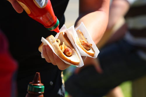 Selective Focus Photo of Person Holding Sausage Sandwiches
