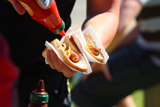 Close-up of a person adding ketchup to hot dogs, highlighting a casual outdoor meal.
