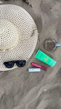Flat lay of beach essentials including sunglasses, sun hat, and sunscreen on sand.