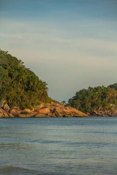 Tranquil view of a lush coastal landscape under a warm sunset with calm waters.