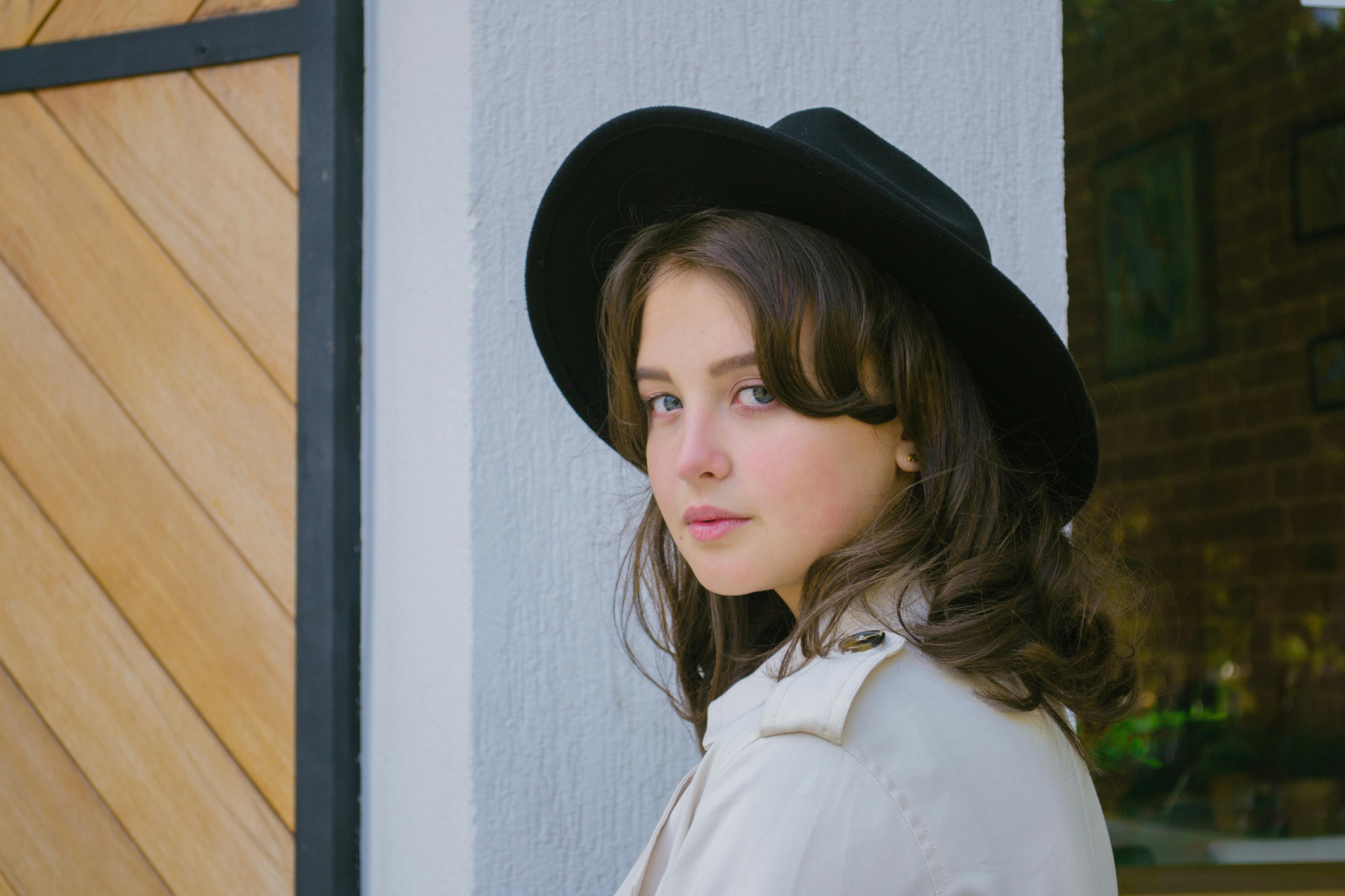 这幅别致的肖像中，一位年轻女子戴着黑色帽子，展现出当代的优雅与风格