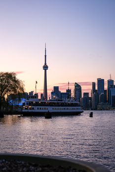 A scenic view of the Toronto skyline with the CN Tower at twilight, featuring a ferry on the water.