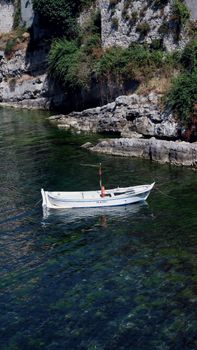 Tranquil white boat floating in a clear rocky cove with lush greenery under bright daylight.