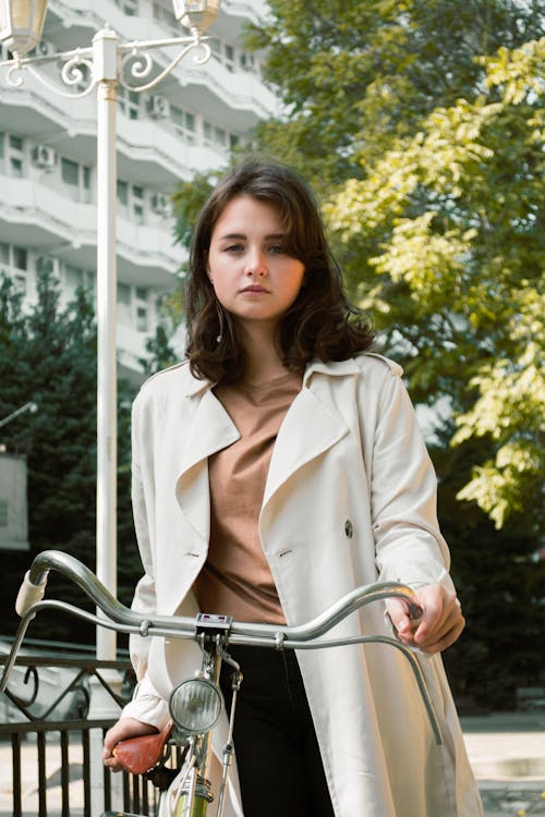 Foto Di Donna Che Indossa Un Trench Bianco Mentre Si Tiene Sulla Bicicletta