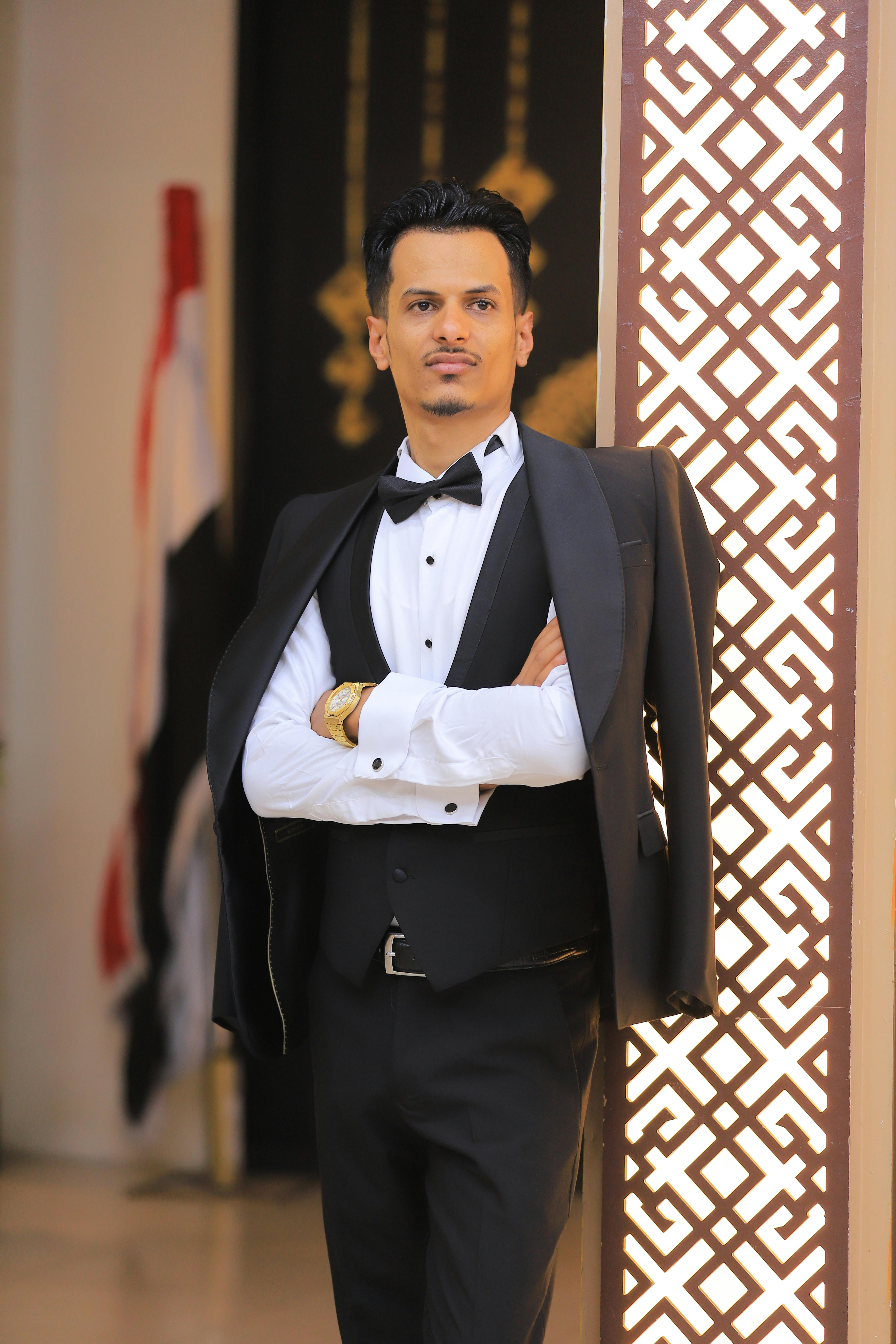A sophisticated man stands confidently in a stylish tuxedo at a formal indoor event.