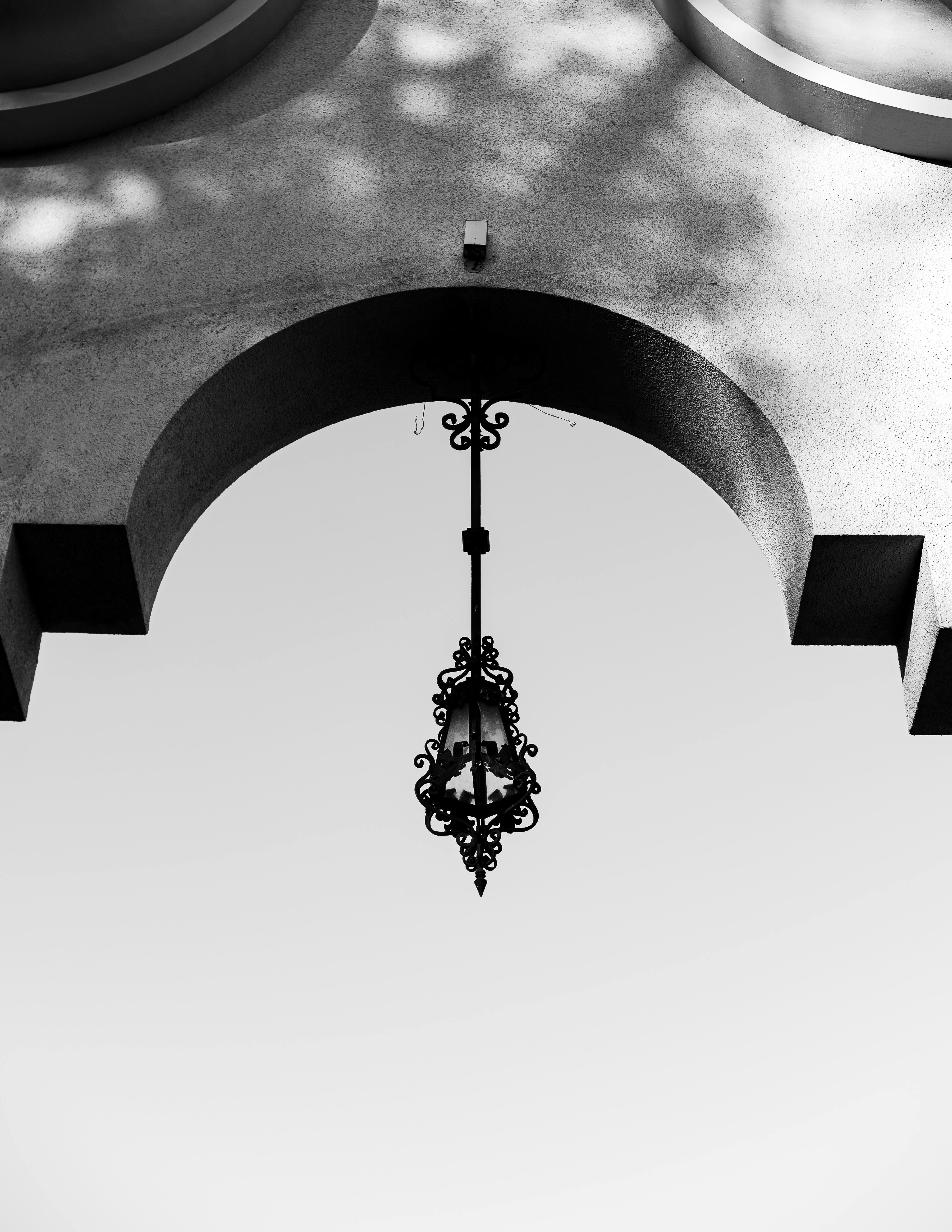 grátis Captura artística de uma luminária ornamentada pendurada em um arco geométrico em monocromático. Foto profissional