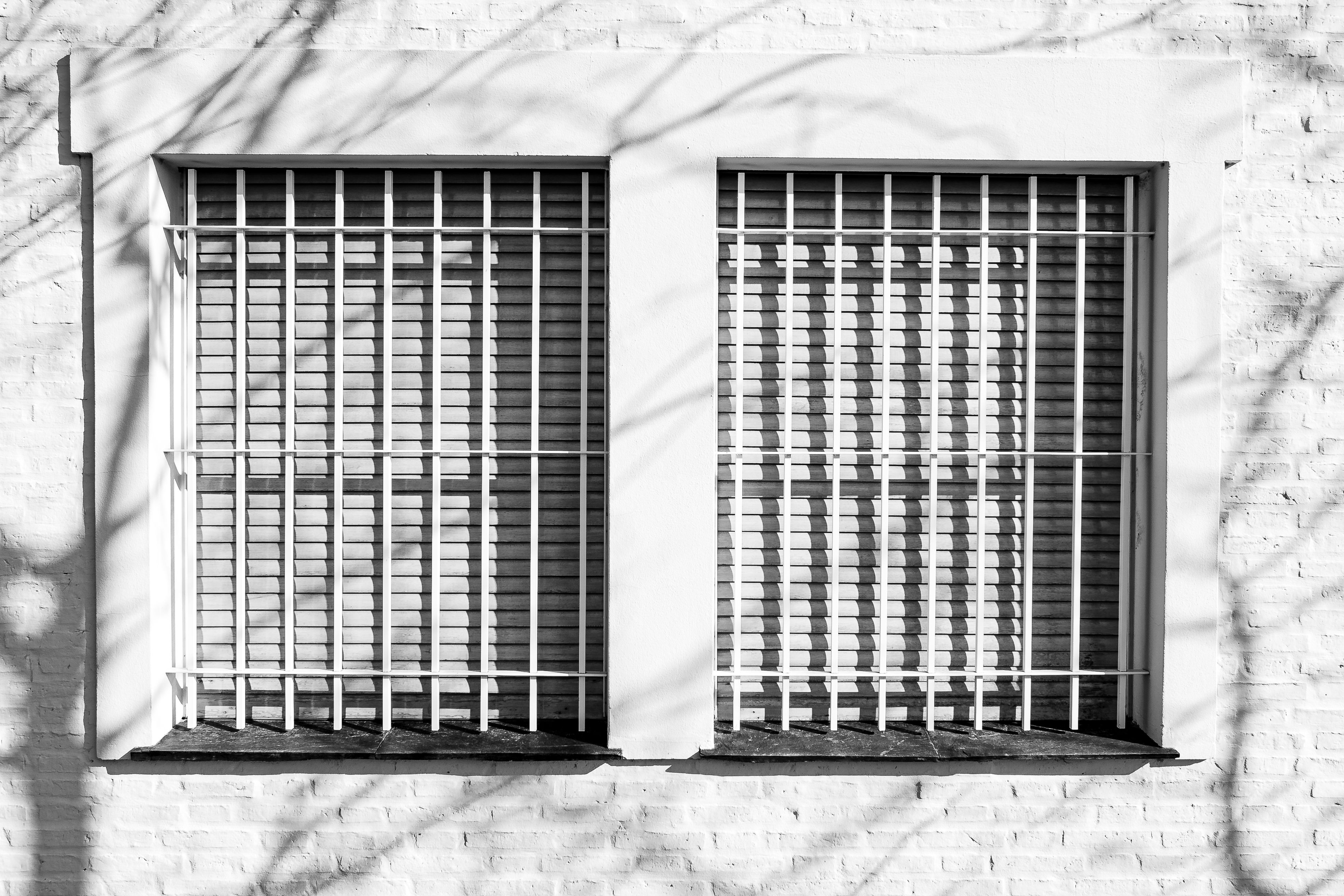 Black and white image of barred windows with shadows in urban setting.