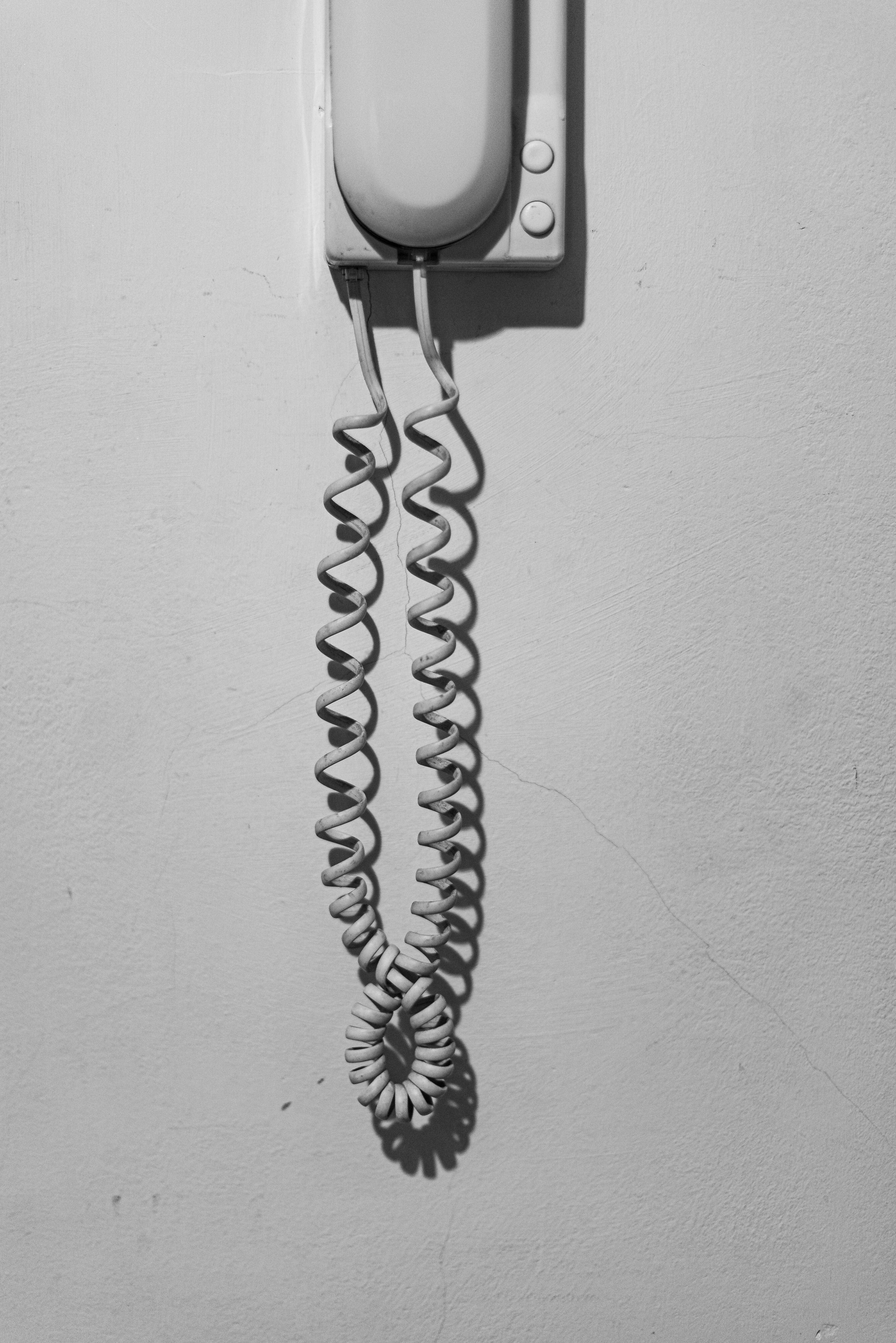 De franc Fotografia en blanc i negre d'un telèfon vintage de paret amb un cable arrissat. Foto d'estoc