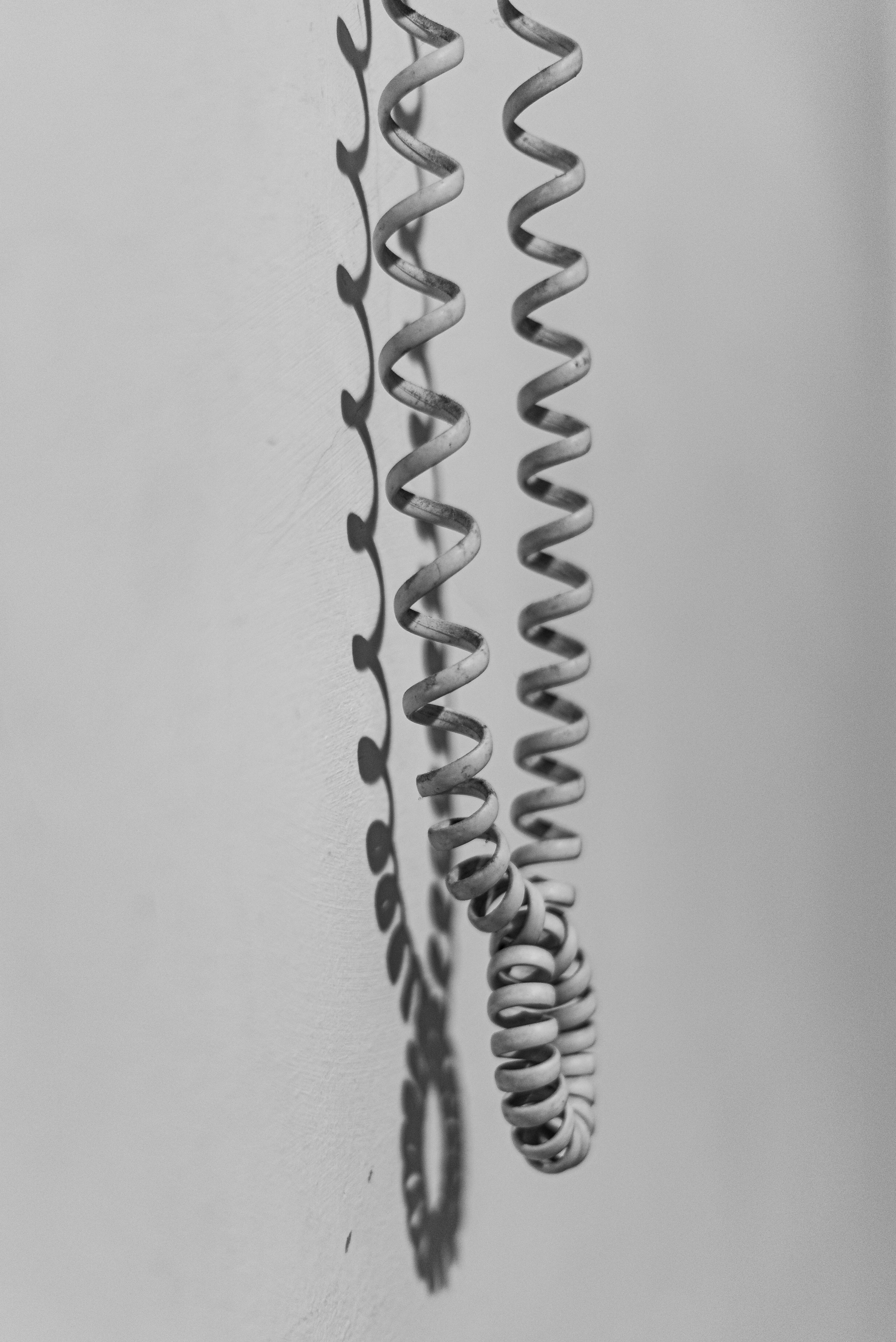 Δωρεάν Μινιμαλιστική ασπρόμαυρη φωτογραφία ενός τυλιγμένου τηλεφωνικού καλωδίου και της σκιάς του σε έναν απλό τοίχο, που αναδεικνύει την αστική απλότητα. Φωτογραφία από στοκ φωτογραφιών