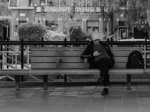 Free Black and white photo of a person sitting on a bench, browsing phone, Bussum, Netherlands. Stock Photo