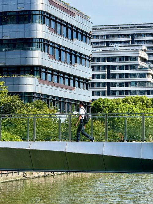 Free A person walks across a sleek, modern bridge set against high-rise buildings in a cityscape. Stock Photo