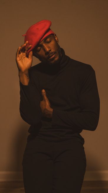 Elegant and contemplative portrait of a man wearing a red beret and black outfit, captured indoors with warm lighting.