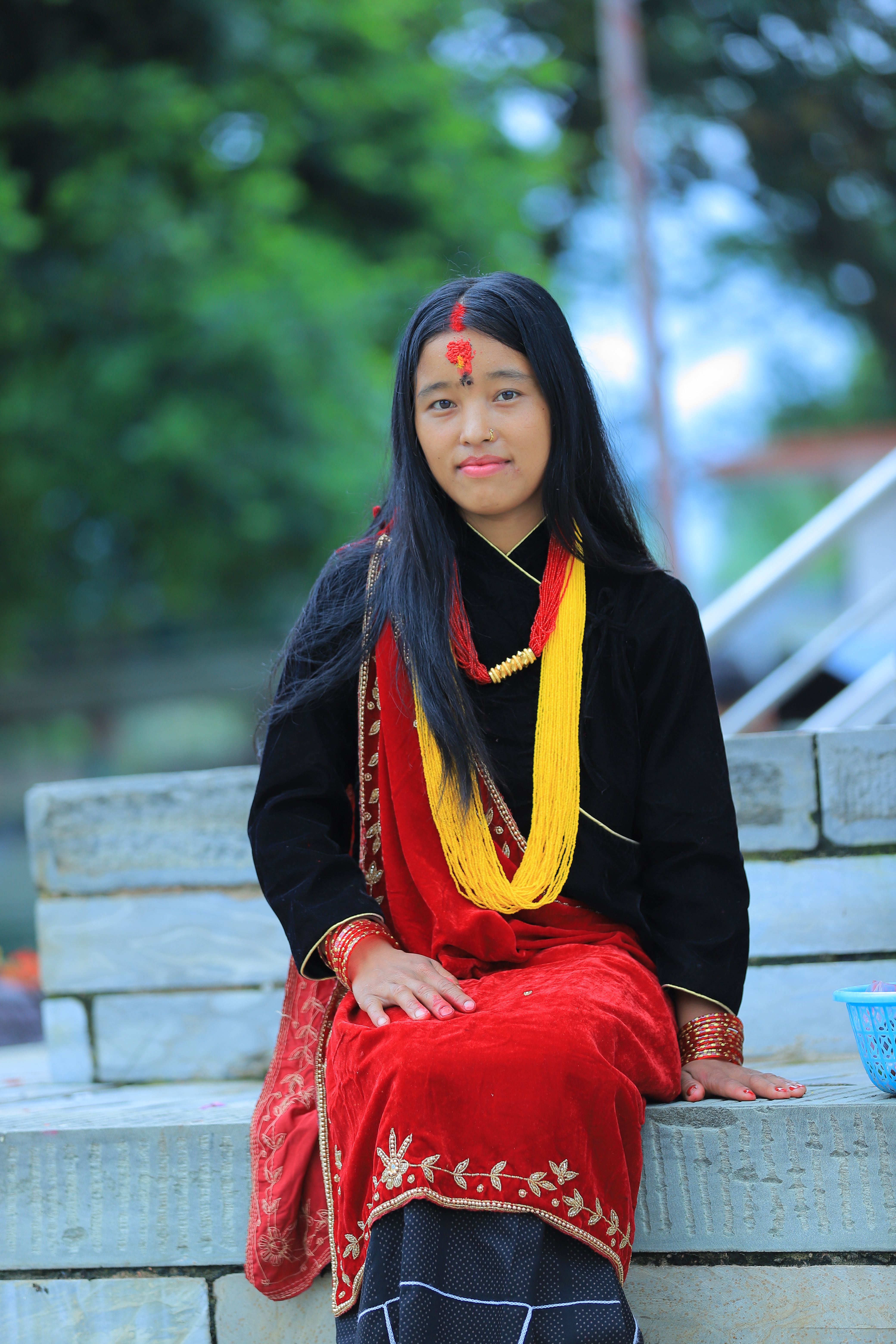A young woman in traditional Nepalese clothing sits outdoors, showcasing vibrant cultural attire.