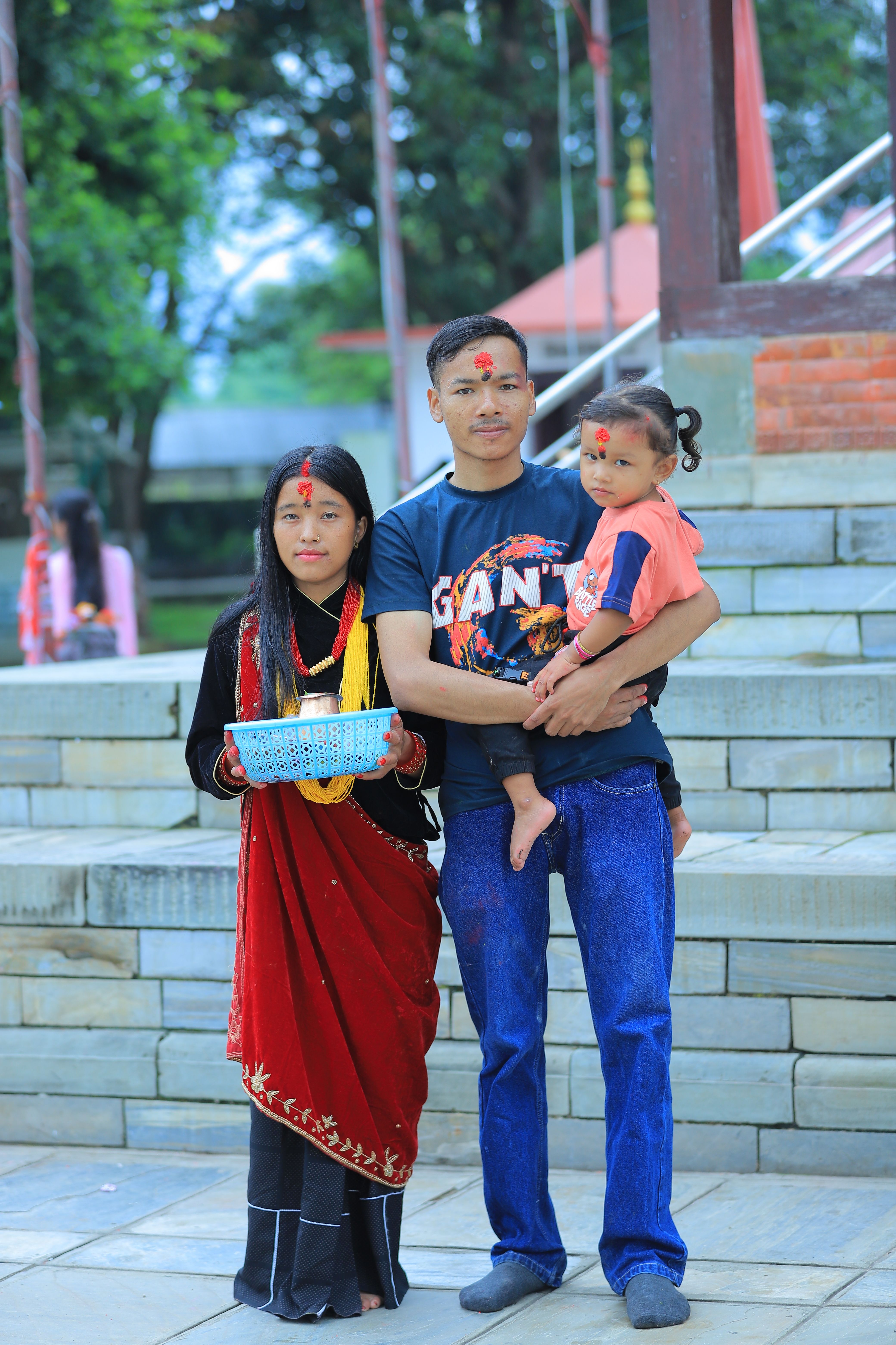 Family posing outdoors at a cultural ceremony with traditional attire and offerings.