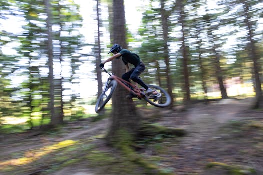 Mountain biker performing a high-speed jump on a forest trail, showcasing action and skill.