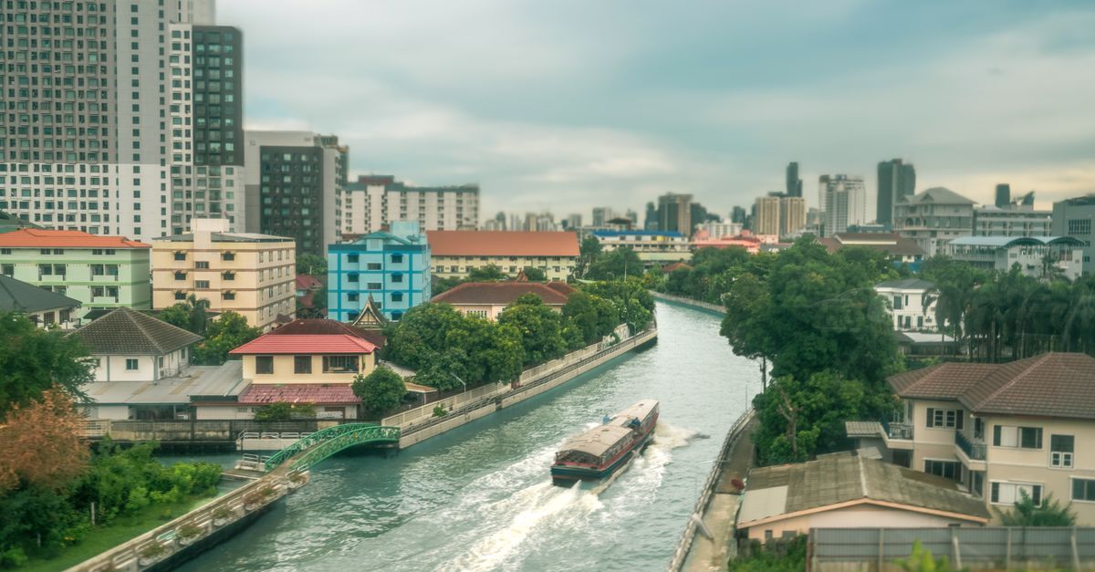 A longtail boat on a Bangkok canal with painted houses along the bank