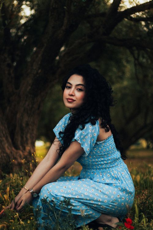 Free Woman in blue floral dress posed gracefully outdoors among trees. Stock Photo