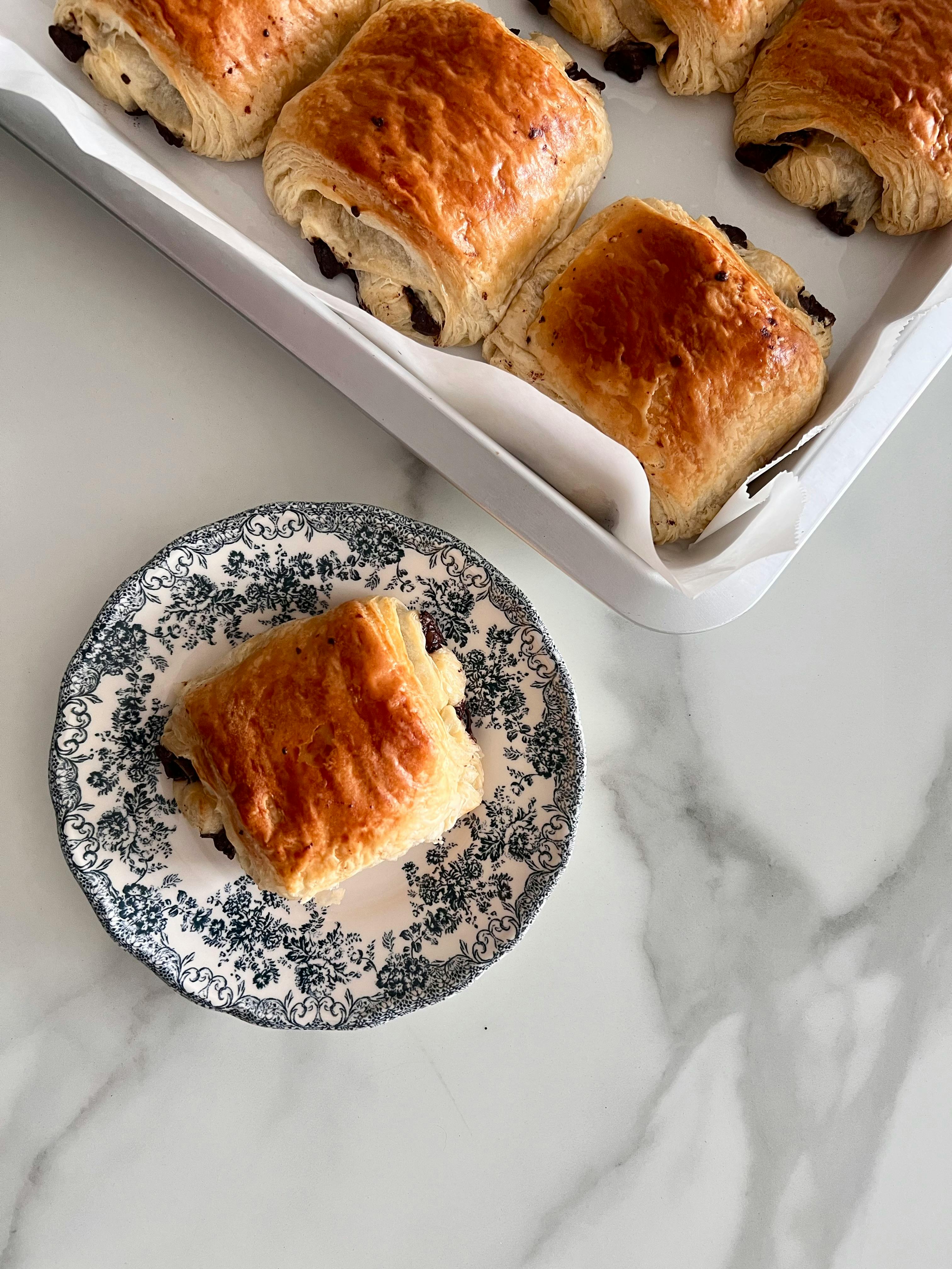 Delicious pain au chocolat pastries fresh from the oven on a decorative plate and marble surface.