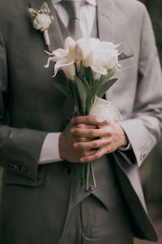 A groom holds a white tulip bouquet, symbolizing purity and love in a serene wedding setting.