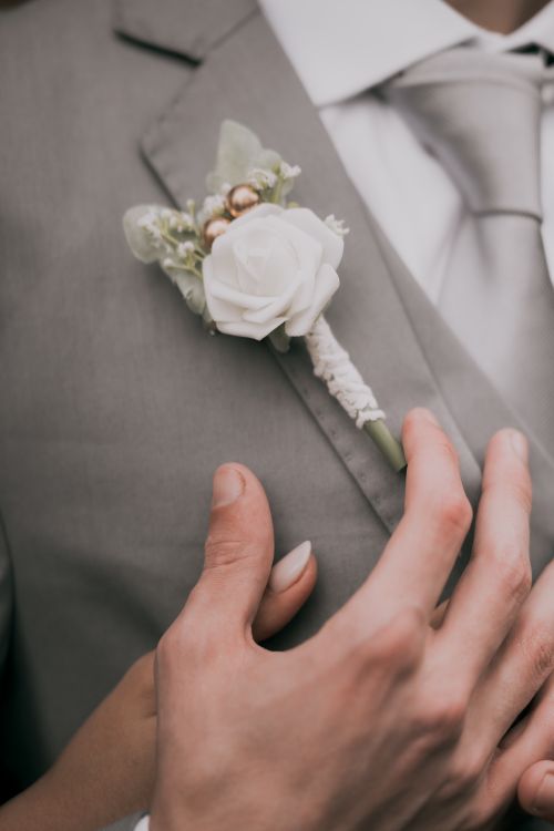 Free Close-up of a white rose boutonniere on a groom's grey suit, symbolizing elegance and love. Stock Photo