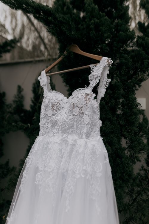 Free A detailed view of a lacy white wedding dress hanging on a wooden hanger outdoors. Stock Photo