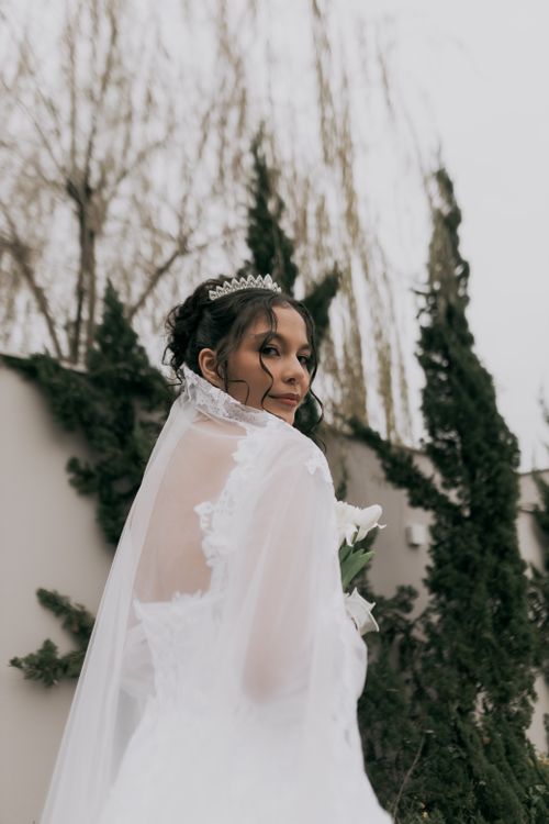 Free Bride in a white gown with tiara, posing gracefully outdoors with greenery backdrop. Stock Photo
