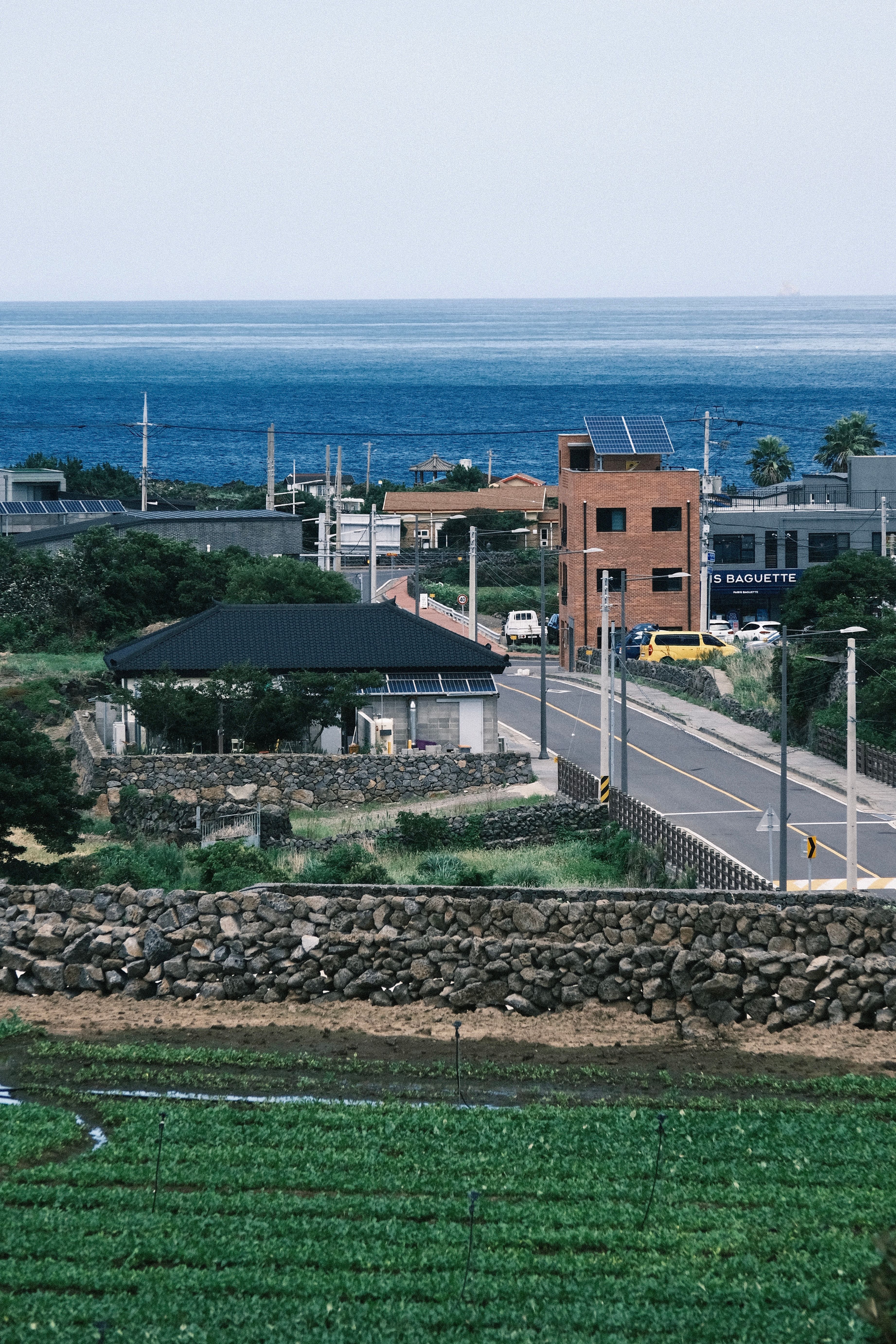 A peaceful coastal village road with ocean views, stone walls, and rural landscape.